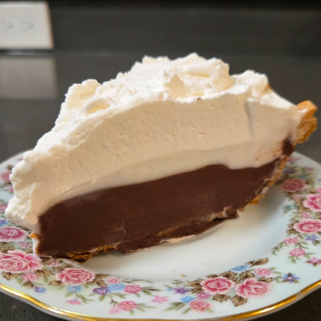 a close up photo of chocolate haupia pie with flaky pie crust, chocolate haupia, coconut haupia, and whipped cream