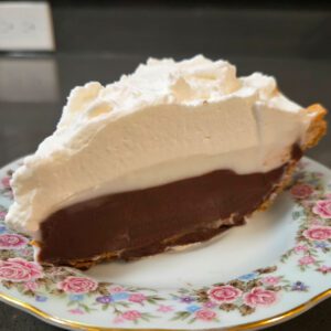 a close up photo of chocolate haupia pie with flaky pie crust, chocolate haupia, coconut haupia, and whipped cream