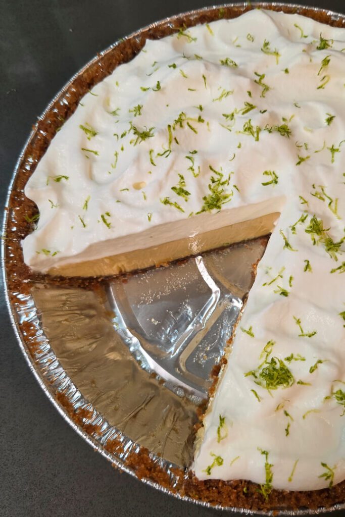 an overhead photo of a key lime pie topped with fluffy whipped cream and lime zest with a slice cut out.