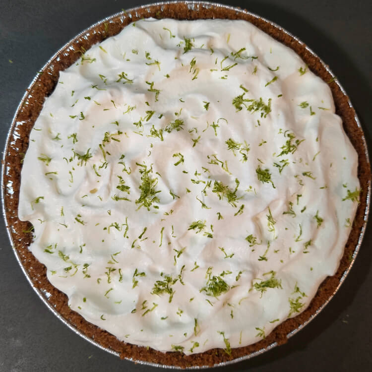 an overhead photo of an unsliced, whole key lime pie topped with whipped cream and green lime zest