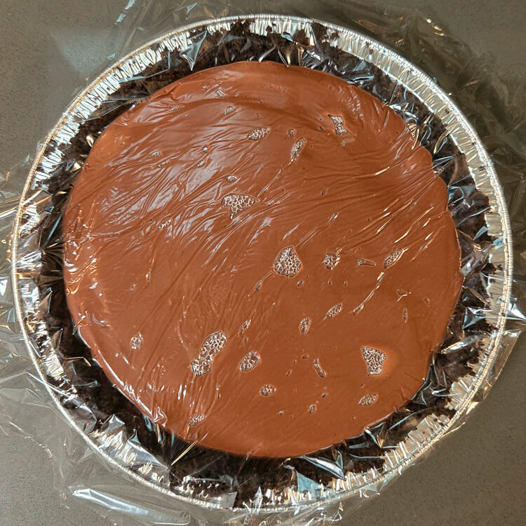 an overhead photo of a mississippi mud pie with plastic pressed to the surface of chocolate pudding to prevent a skin from forming