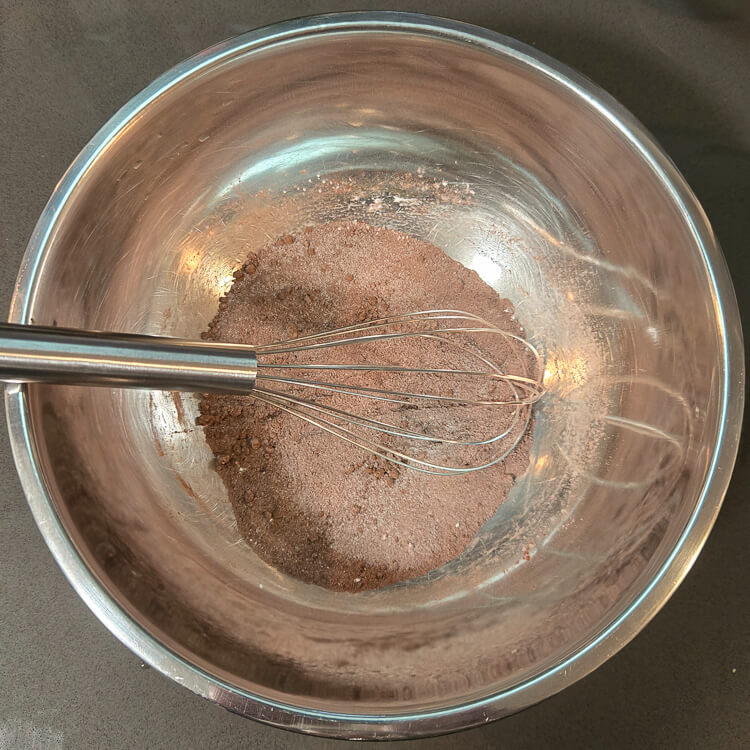 dry ingredients (cocoa powder, sugar, and cornstarch) whisked together in a metal mixing bowl with a metal whisk