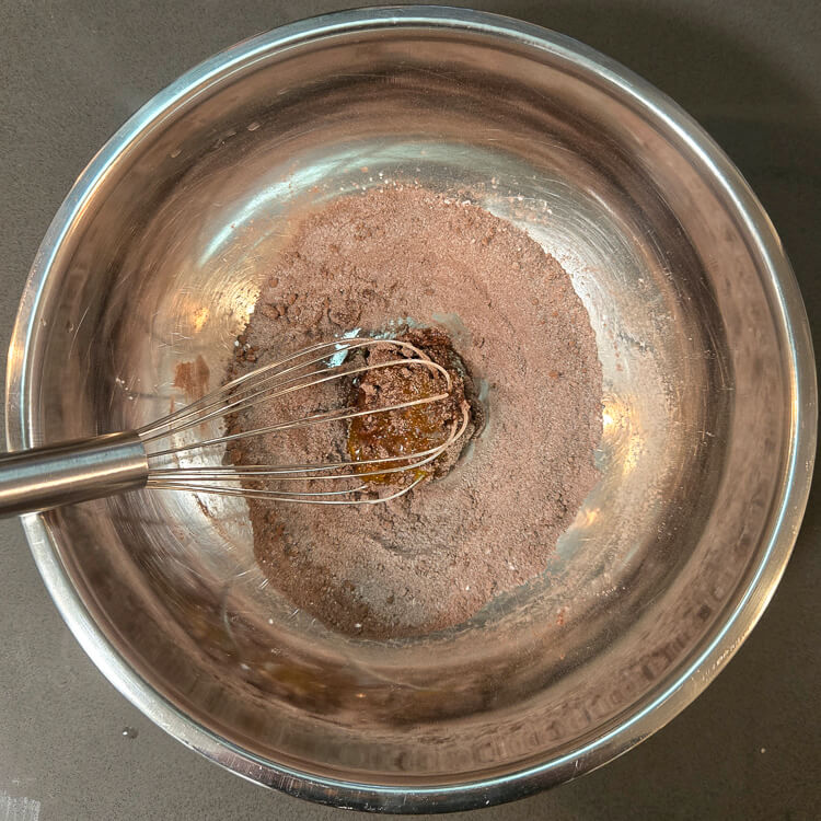 dry ingredients (cocoa powder, cornstarch, and sugar) whisked together with an egg yolk in a metal mixing bowl with a metal whisk