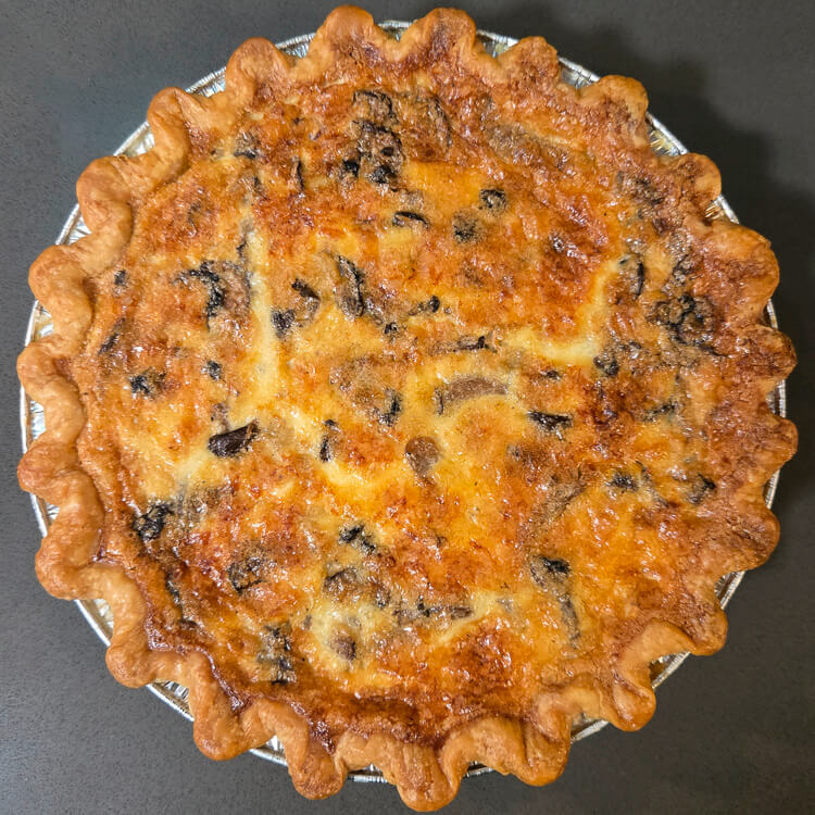 an overhead photo of a golden brown baked mushroom quiche in a golden crimped flaky pie crust
