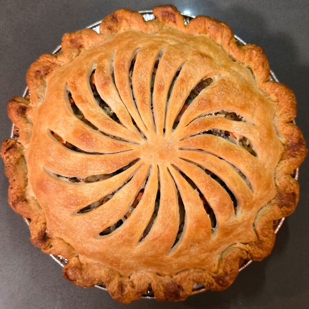 an overhead photo of an Alaskan salmon pie (pirok) with a golden brown crust, with vents cut in a pinwheel design
