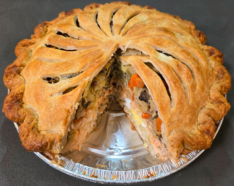 a photo showing a cross section of alaskan pirok after a slice has been cut out showing the layers: rice, salmon, vegetables, and eggs