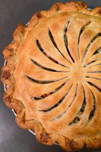 a close-up overhead photo of an Alaskan salmon pie (pirok) with a golden brown crust, with vents cut in a pinwheel design