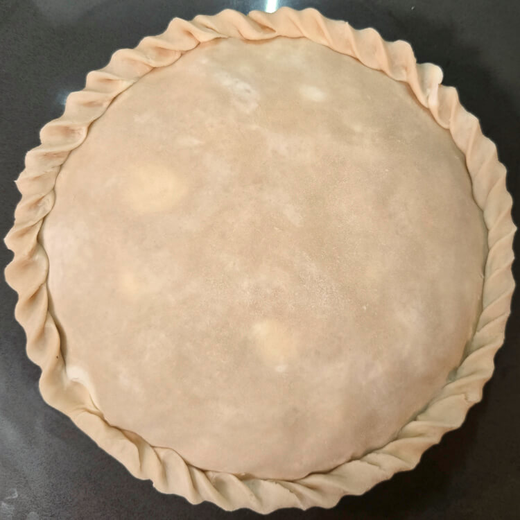 an overhead photo of a double-crusted pie after being sealed and before being fluted. The edge has been rolled into a rope.