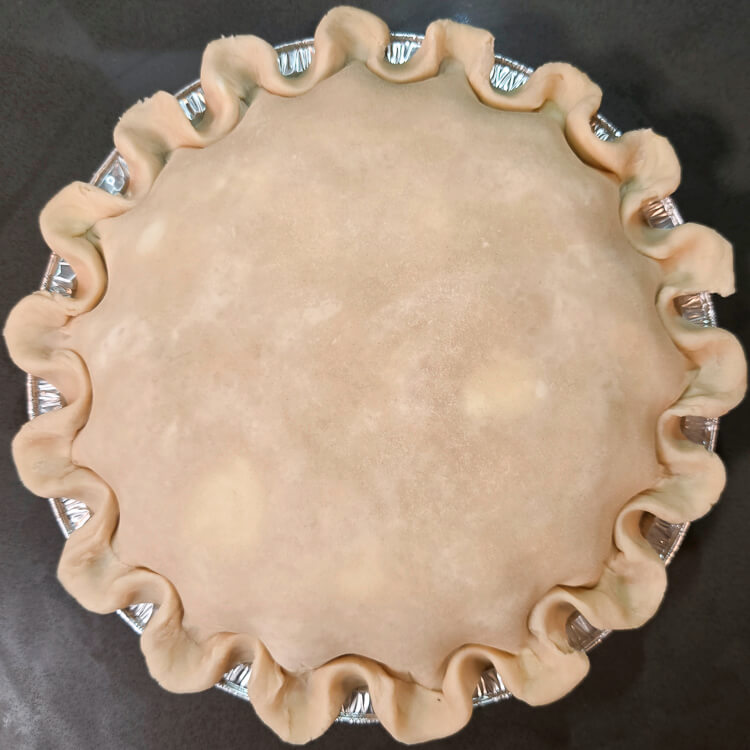 an overhead photo of a double-crusted pie just after being sealed showing defined fluted edges