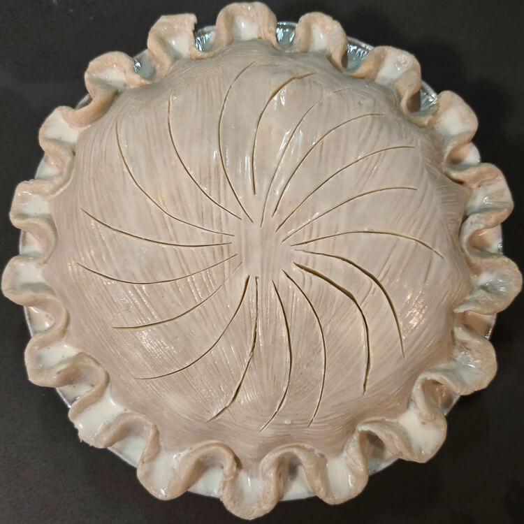 an overhead photo of a double-crusted alaskan salmon pie before it is baked showing flutes, a pinwheel design for the vents, and washed with cream for color