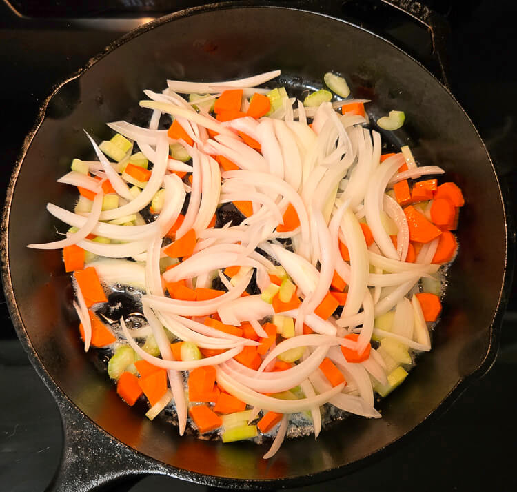 diced carrots and celery, and sliced onions being sauteed in a cast iron skillet