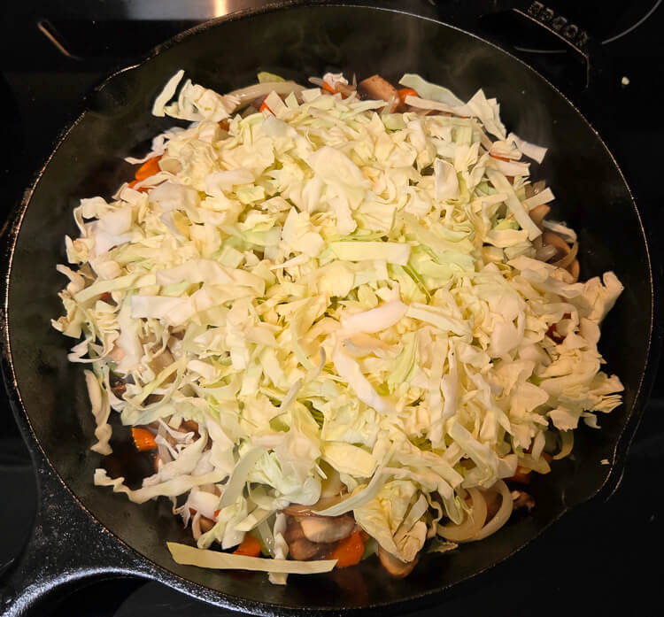vegetables being sauteed in a cast iron pan for alaskan salmon pie: cabbage has just been added to an assortment of vegetables