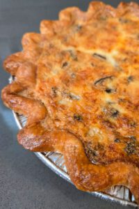 a close up photo of a baked mushroom quiche with a golden-brown crimped pie crust and golden quiche custard