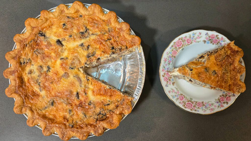 an overhead photo of both a whole mushroom quiche with a slice cut out and the slice placed next to it on an antique floral plate.