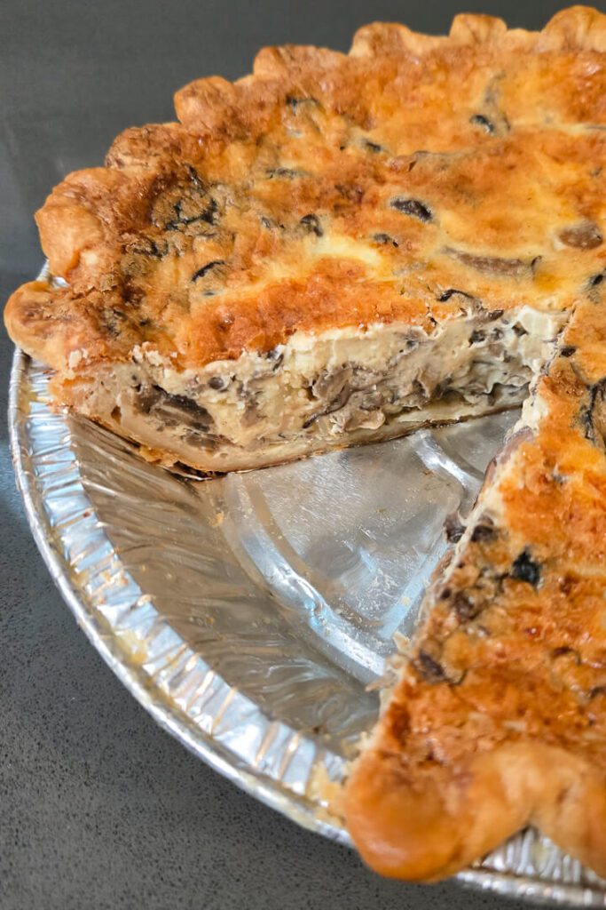 a close up photo of a mushroom quiche with a slice cut out so you can see a close-up cross section with creamy and cheesy custard and sauteed mushrooms