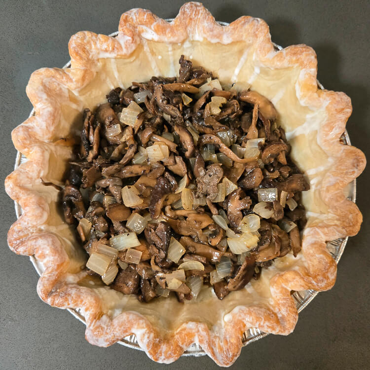 an overhead photo of a mushroom quiche before adding the quiche filling. A crimped blind-baked pie crust filled with sauteed mushroom and onions