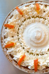 sour orange pie recipe. close up overhead photo of a sour orange pie topped with piped whipped cream and orange slices