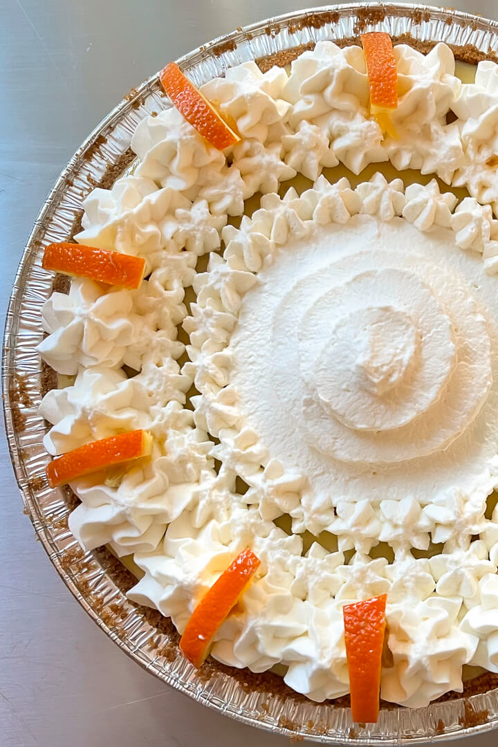 sour orange pie recipe. close up overhead photo of a sour orange pie topped with piped whipped cream and orange slices