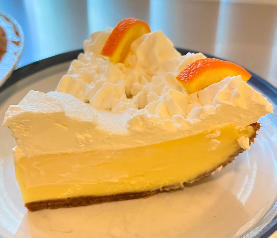 a close up photo of a slice of sour orange pie with piped whipped cream on top and decorative orange slices