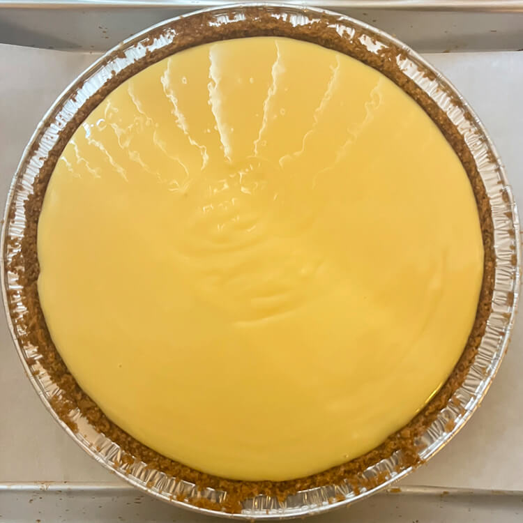 an overhead photo of a whole, unbaked sour orange pie showing the unbaked yellow-orange custard in a graham cracker crust in a metal pie tin