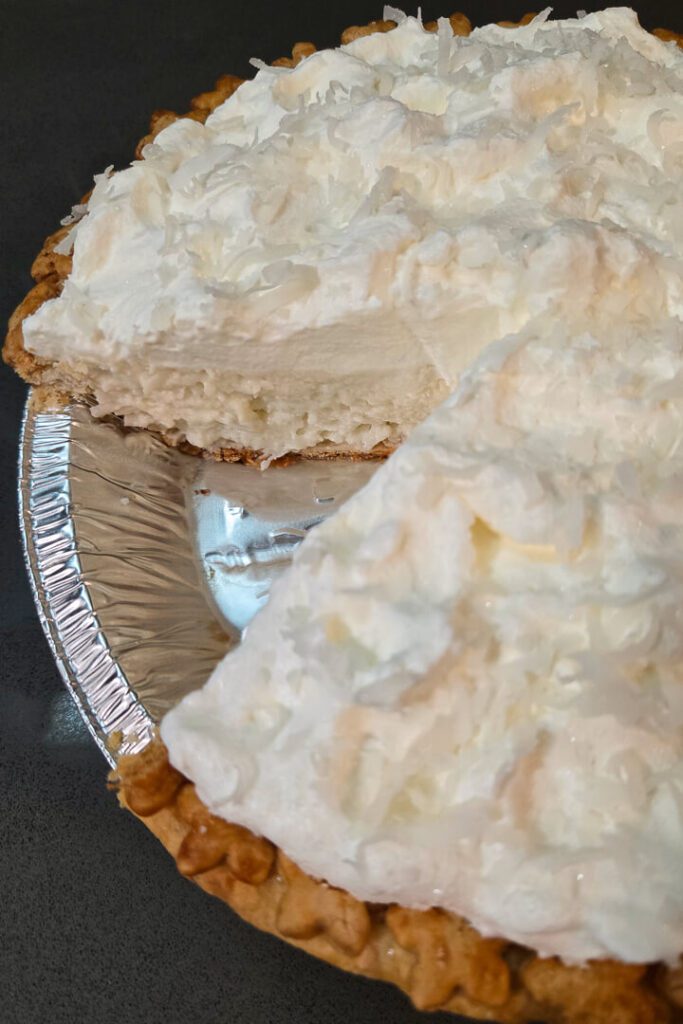 White christmas pie close up showing a golden pie crust with star cutouts topped with whipped cream, shredded coconuts, and sanding sugar with a slice cut out showing the fluffy white cloud-like filling inside