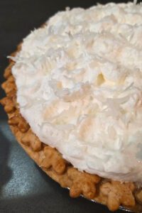 White christmas pie close up showing a golden pie crust with star cutouts topped with whipped cream, shredded coconuts, and sanding sugar
