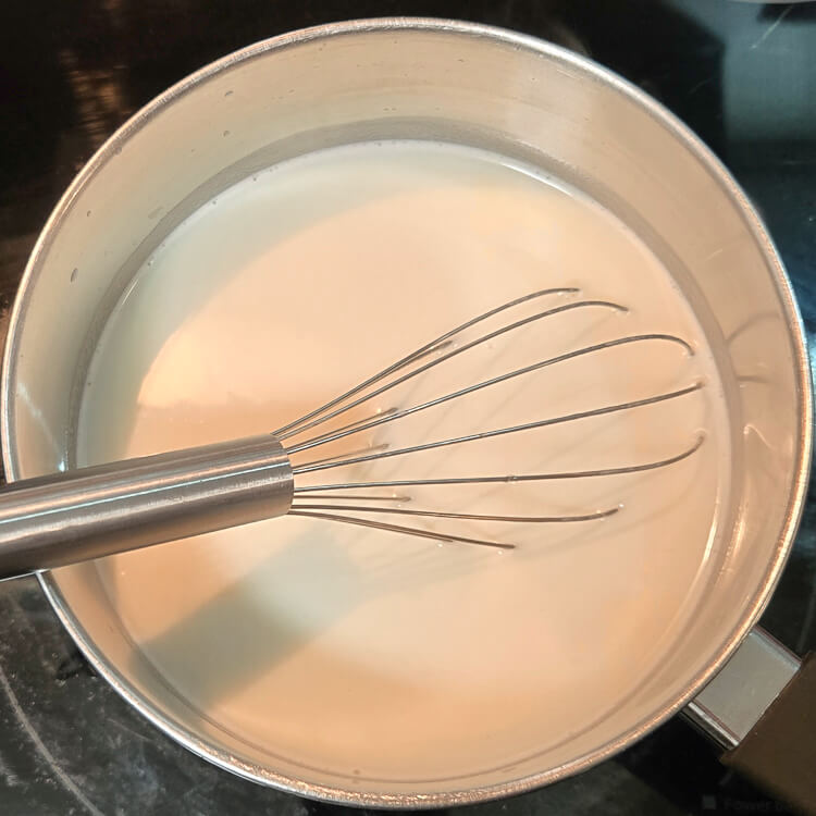 milk and sugar being heated on a stove top with a metal whisk pictured