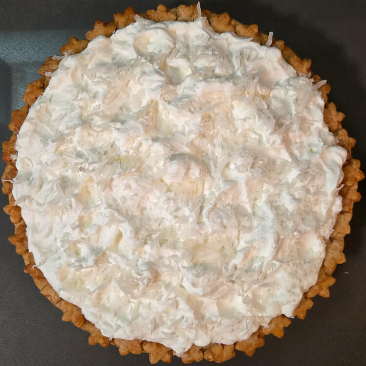 an overhead photo of a white christmas pie topped with whipped cream and shredded coconut to look like snow