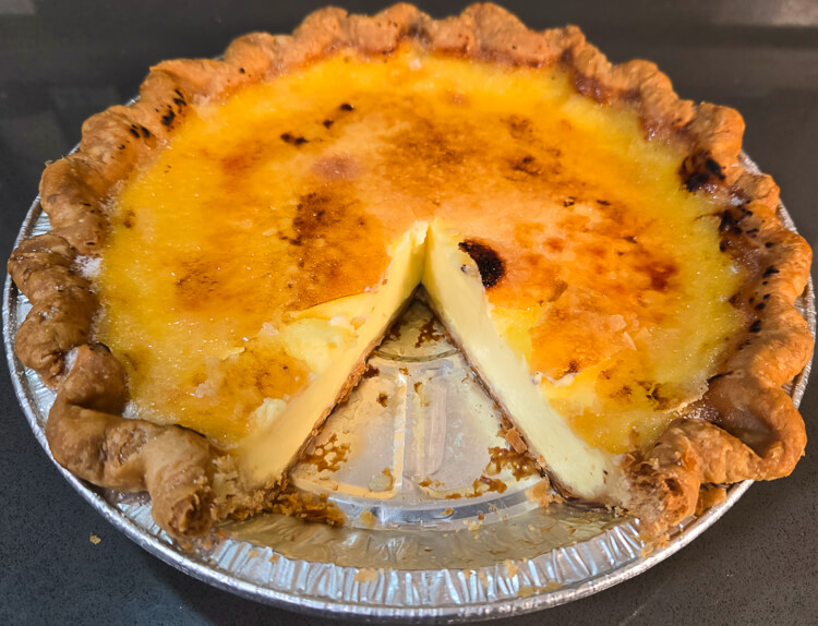 a whole crème brûlée pie with a slice cut out showing a golden caramel top with a rich custard filling