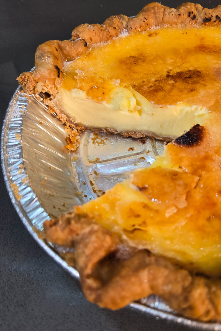 close up photo of a crème brûlée pie with a slice cut out showing a rich vanilla custard and a cracked caramel topping
