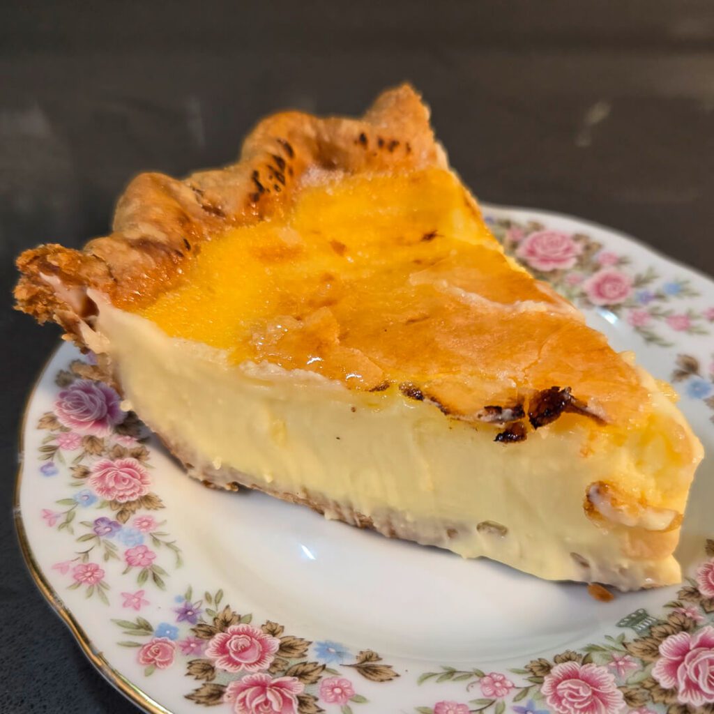 a close up photo of a slice of crème brûlée pie on an antique floral plate with a cracked golden caramel top
