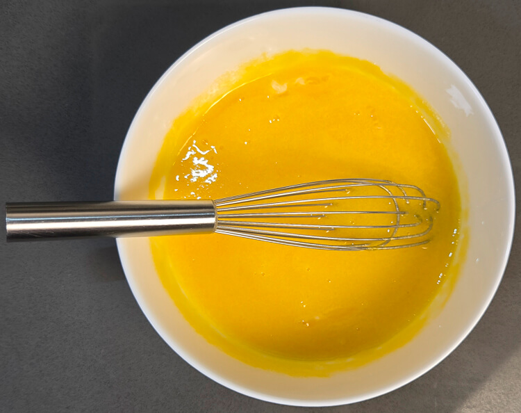 egg yolks and sugar whisked together in a white bowl with a metal whisk
