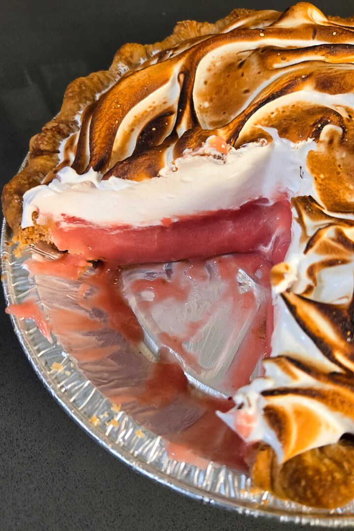 close up photo of a cranberry meringue pie with a slice cut out showing the red cranberry curd and the fluffy toasted meringue