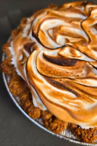 close up photograph of a pie in a golden flaky fluted pie crust topped with golden toasted meringue
