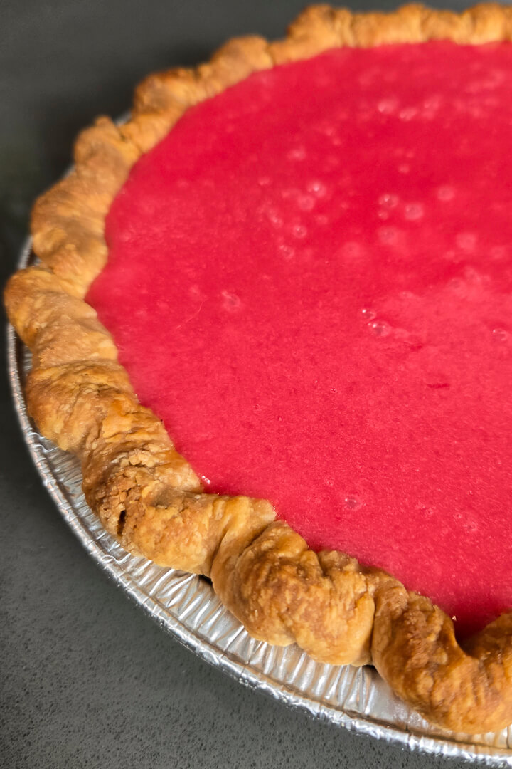 close up photo of vibrant bright red cranberry curd set in a golden brown fluted pie crust