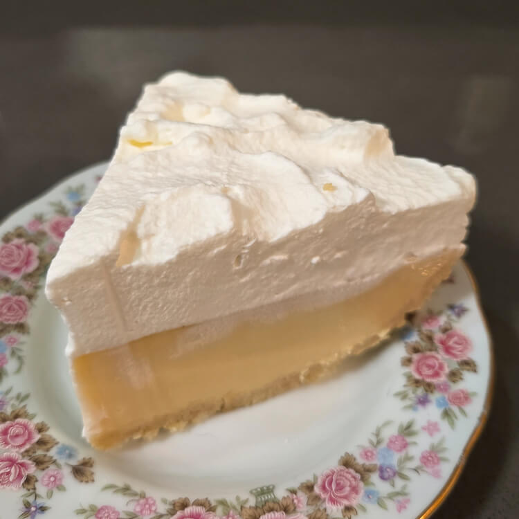 a close up photo of a slice of atlantic beach pie showing the slatine cracker crust, lemon-lime filling, and whipped cream topping on an antique floral plate