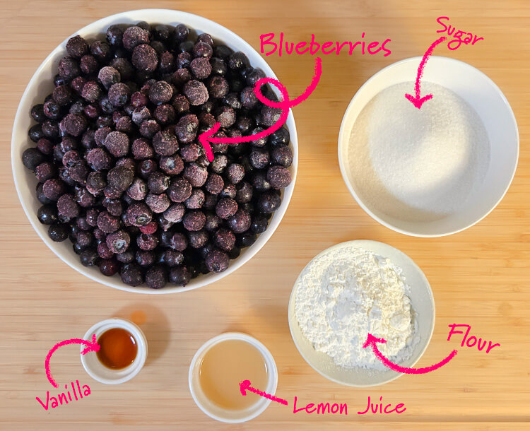 ingredients for blueberry pie filling on a cutting board with text labels: blueberries, sugar, vanilla, lemon juice, and flour