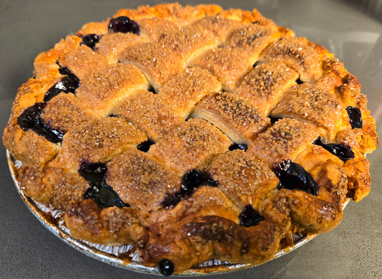 a photo of a blueberry pie in a golden crust with juicy filling with a lattice top