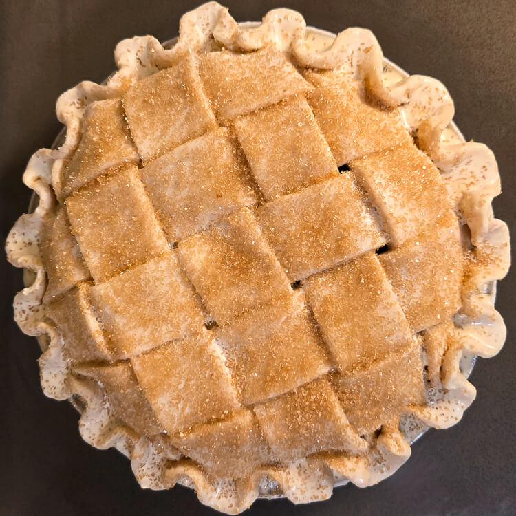 an overhead photo of a blueberry pie topped with lattice crust and sugar with crimped pie crust edges before baking