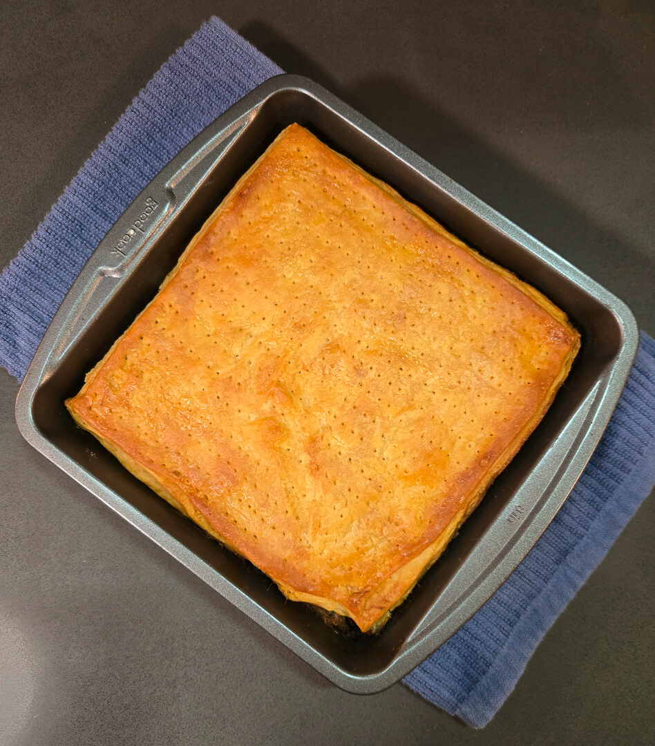 overhead photo of a baked chester cake (gur cake) in a square baking pan with a golden brown top crust
