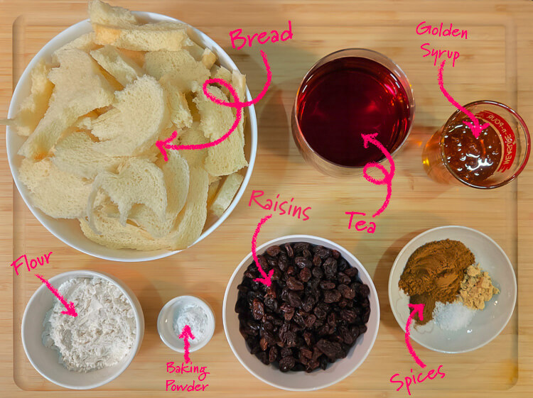 ingredients for chester cake (gur cake) laid out on a cutting board with text labels: bread, tea, golden syrup, raisins, flour, baking powder, spices