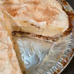 a whole eggnog cream pie in a gingersnap crust with a slice cut out and text overlay that reads "Eggnog Cream Pie"