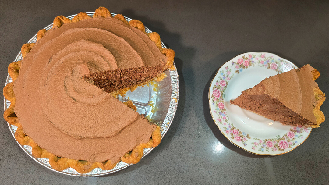 an overhead photo of a French silk pie (chocolate mousse pie) with a slice cut out and placed next to it on a floral plate