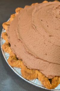 a close up photo of a French silk pie with fluffy chocolate mousse filling a golden brown baked crimped pie crust