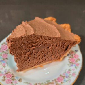 a close up photo of a slice of French silk pie (chocolate mousse pie) showing fluffy chocolate mousse in a golden brown pie crust on an antique floral plate