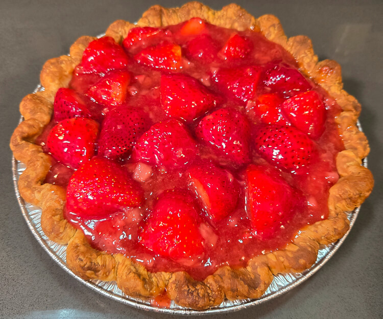 a photo of a fresh strawberry pie with glossy strawberry glaze in a crimped pie crust before the strawberry glaze has fully set