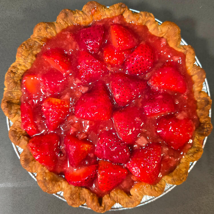 an overhead photo of a fresh strawberry pie with glossy red strawberry glaze in a crimped pie crust