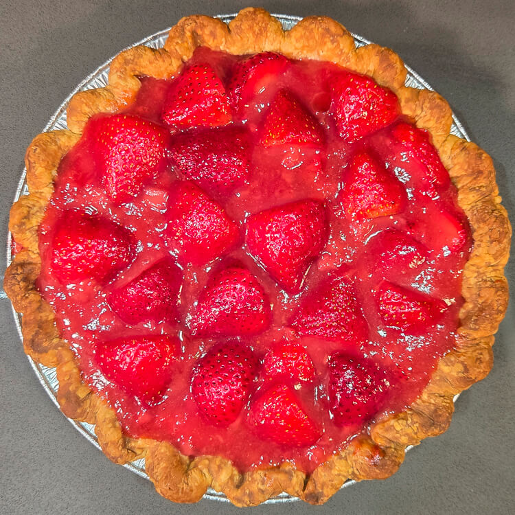 an overhead photo of a fresh strawberry pie with glossy red strawberry glaze in a crimped pie crust