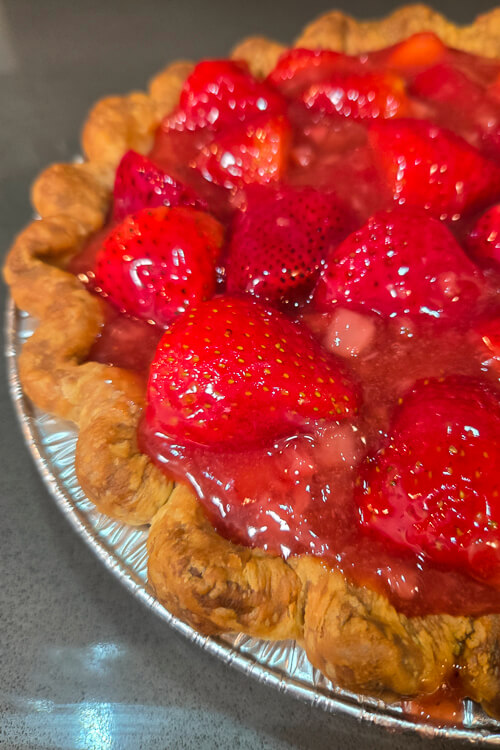 a close up photo of a fresh strawberry pie with glossy red strawberry glaze in a crimped pie crust