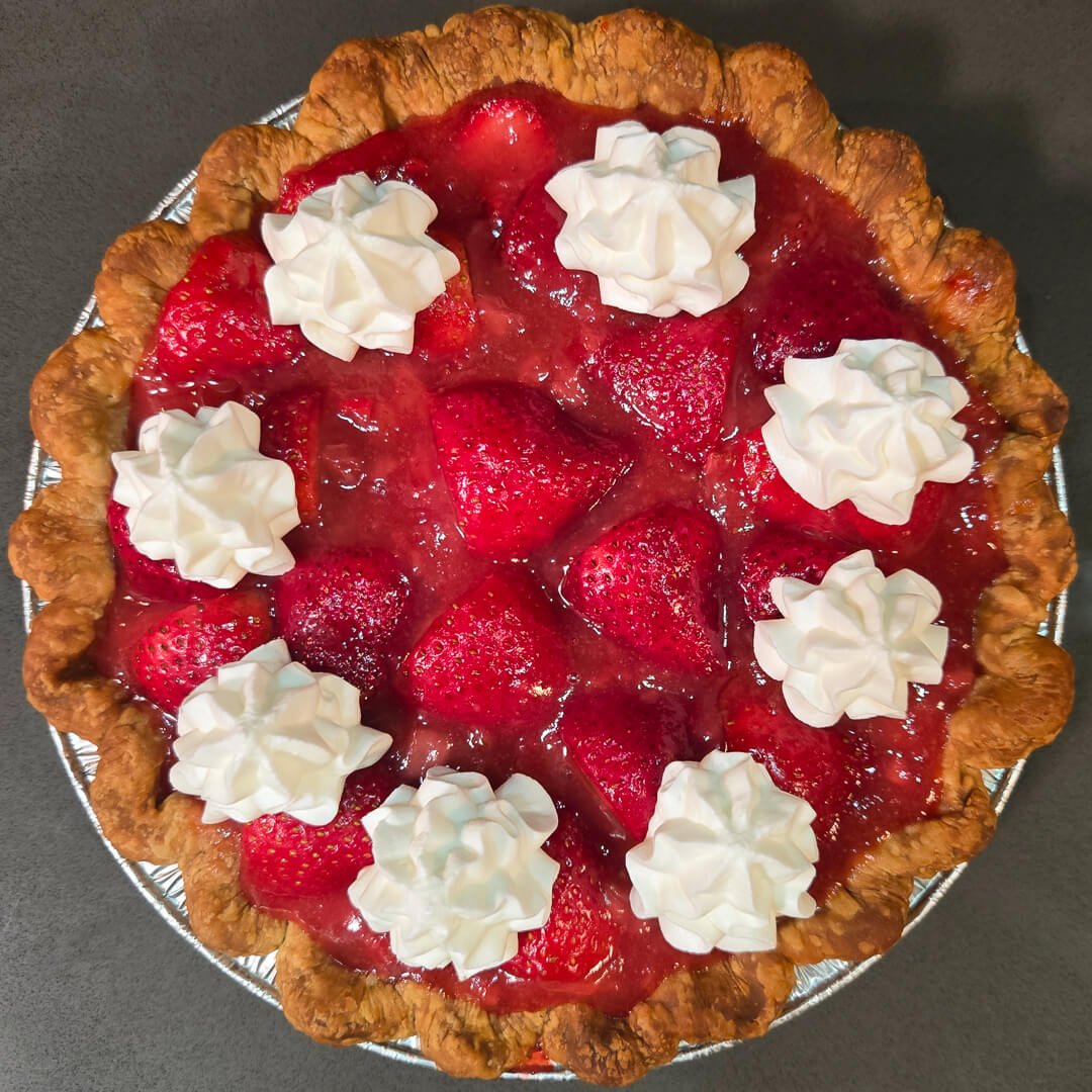 an overhead photo of fresh strawberry pie with glossy red glaze topped with piped whipped cream in a crimped pie crust